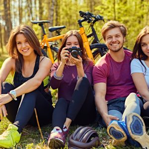 Groupe of people relaxing after bicycle ride in a forest. Female taking picture with digital compact photo camera.